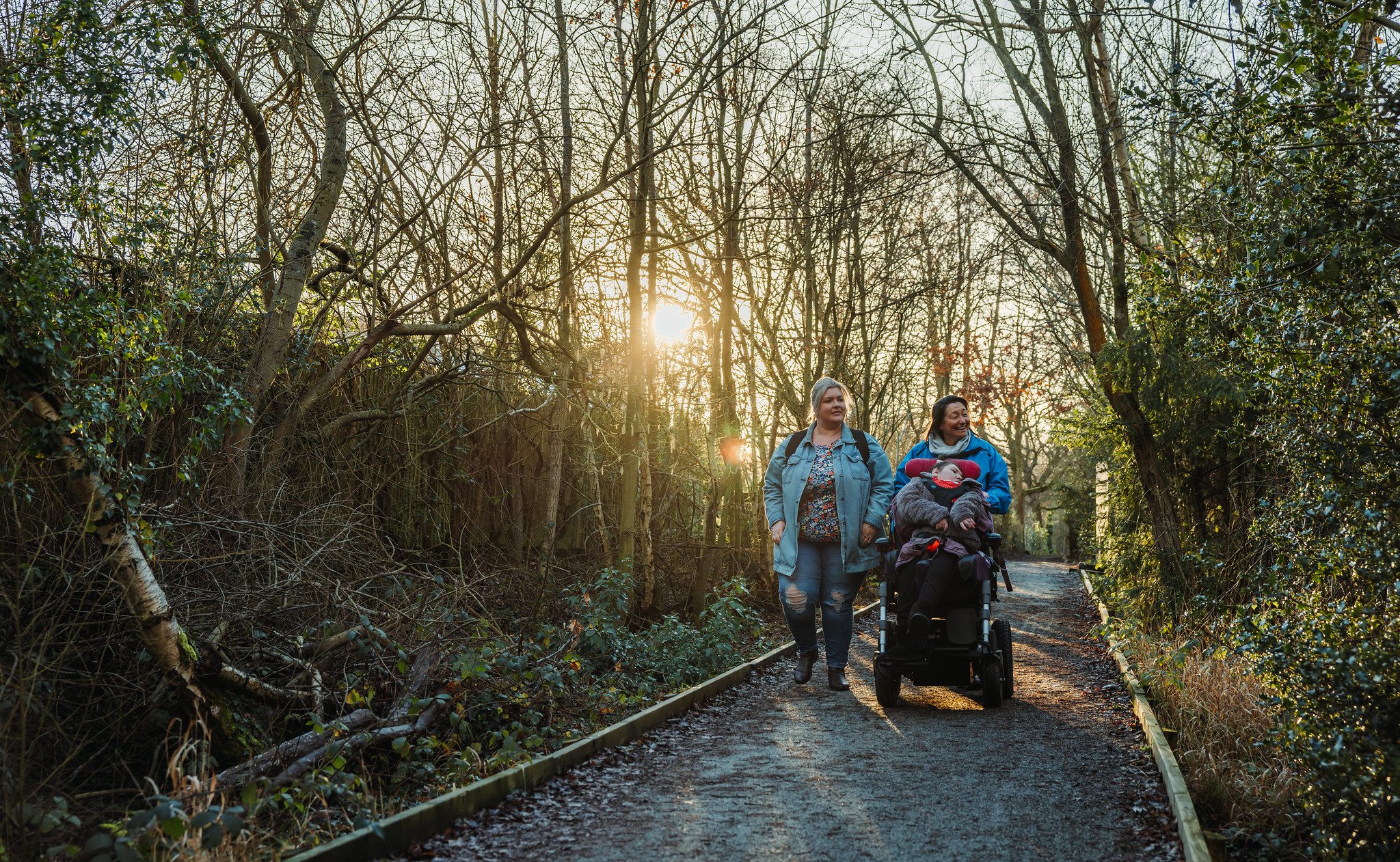 Two women and girl in wheelchair walking along footpath in winter