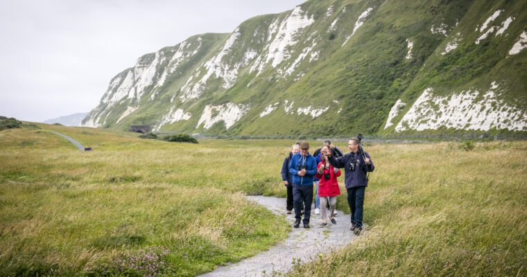 Group of people walking on path, at Samphire Hoe with cliffs to right.
