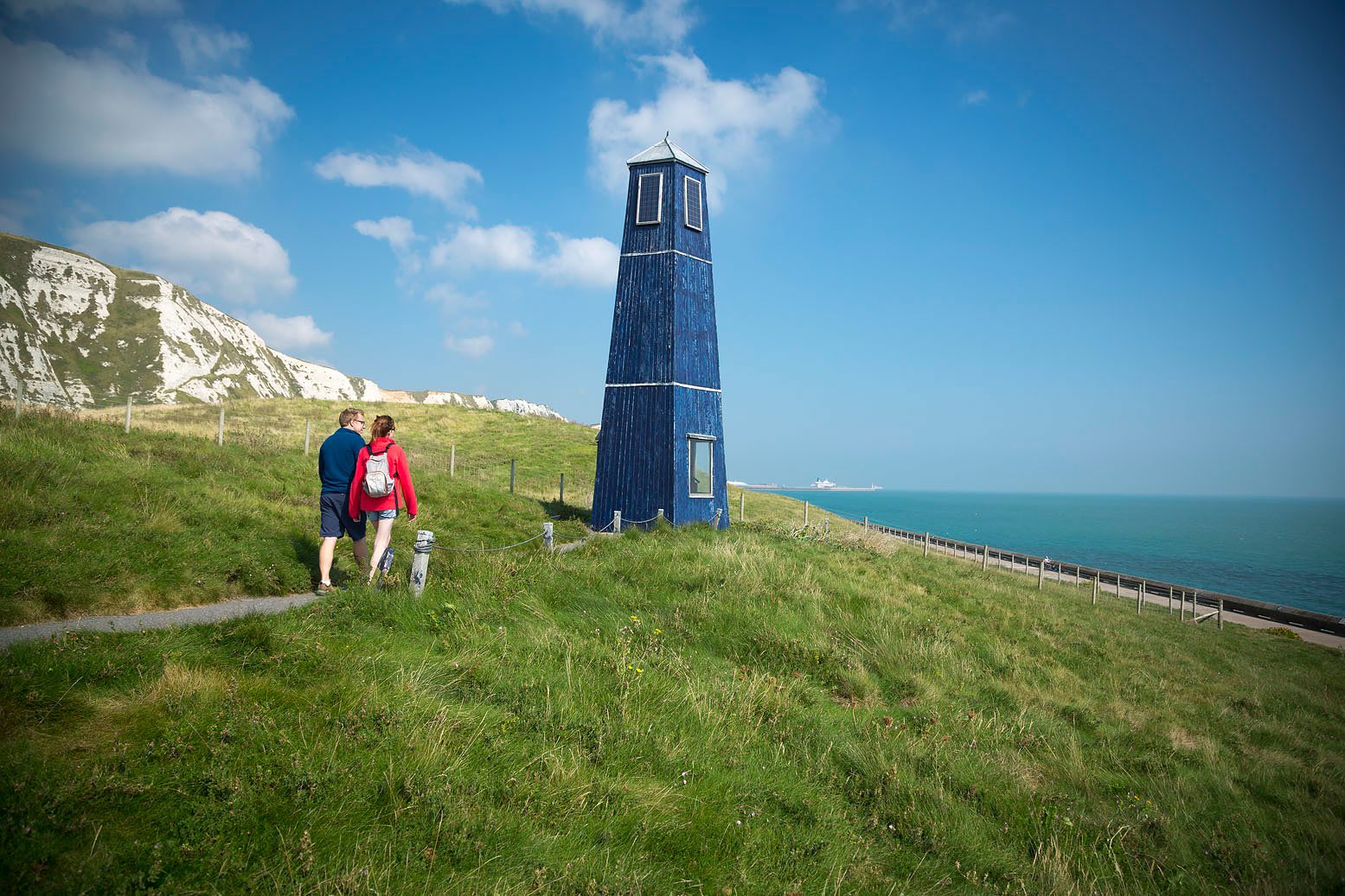 Couple walk towards radio tower beneath white cliffs of Dover