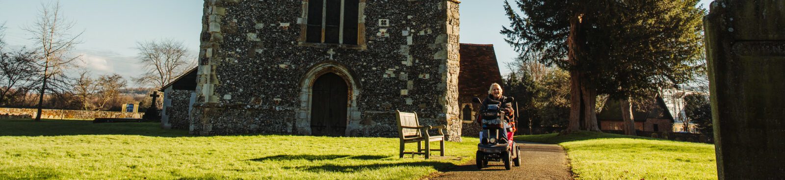 Person in a mobility scooter riding along path in front of Chilham church