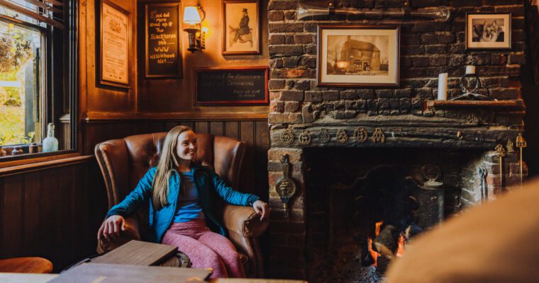 Woman sitting in chesterfield arm chair in corner of cosy traditional pub