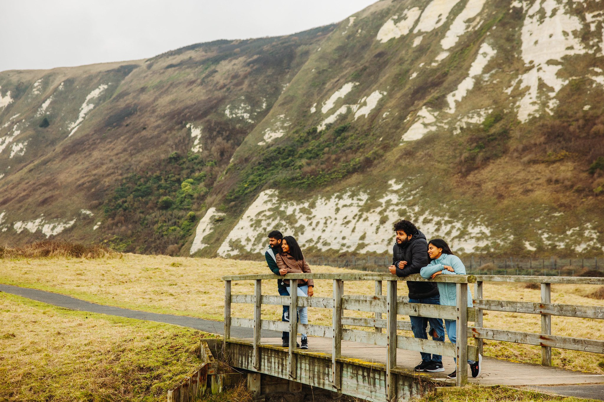 Four Asian people leaning on the side of a bridge at the foot of the white cliffs