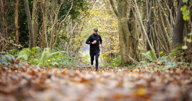 Man running along woodland path in winter with leaves on the ground