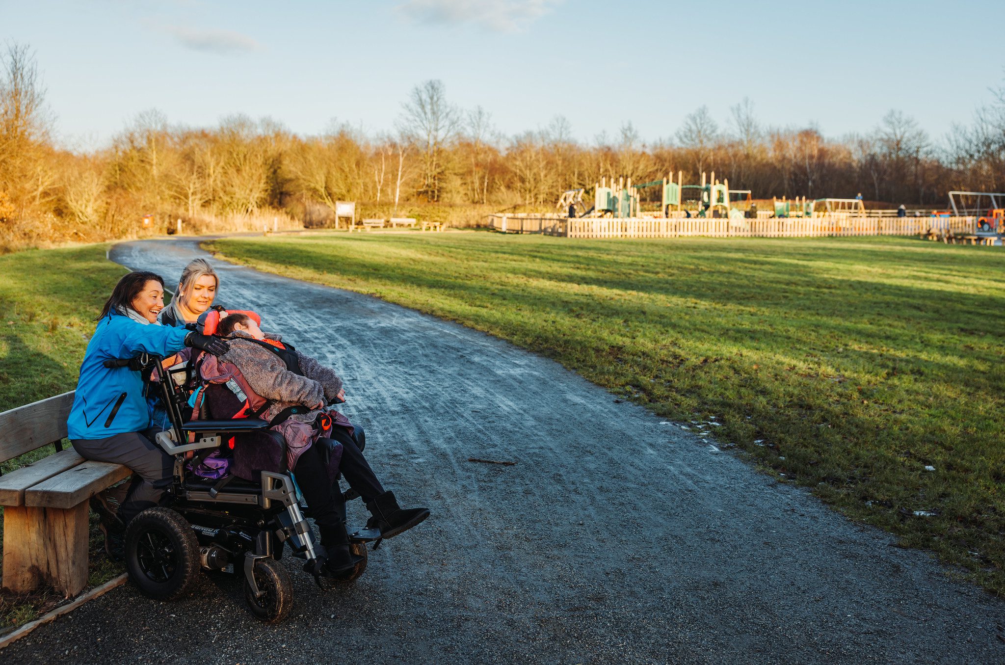 People of all abilities sitting in winter coats in front of distant play area