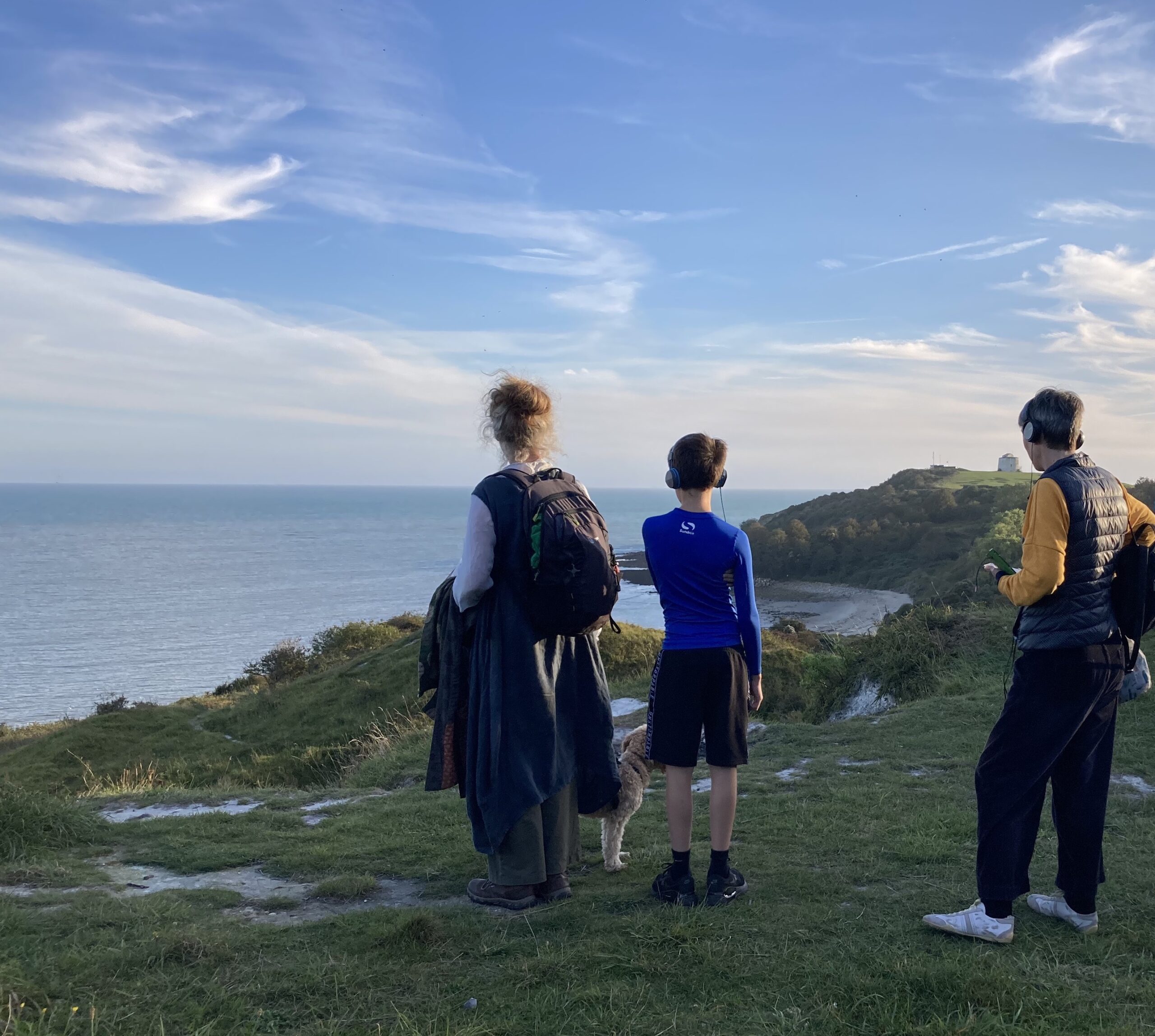 Three people wearing headphones looking out to sea.