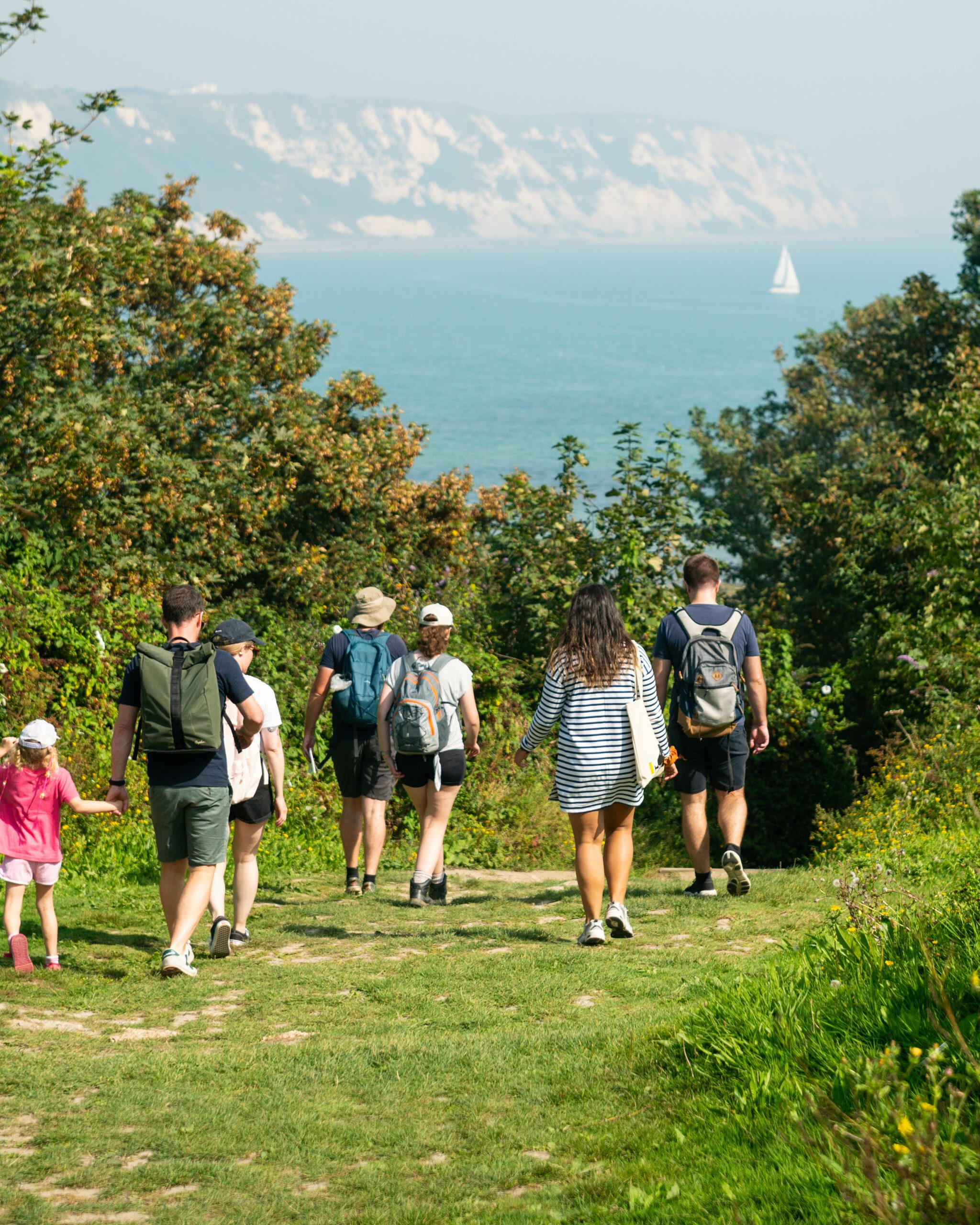 Group of people of all ages walking through grassland towards sea