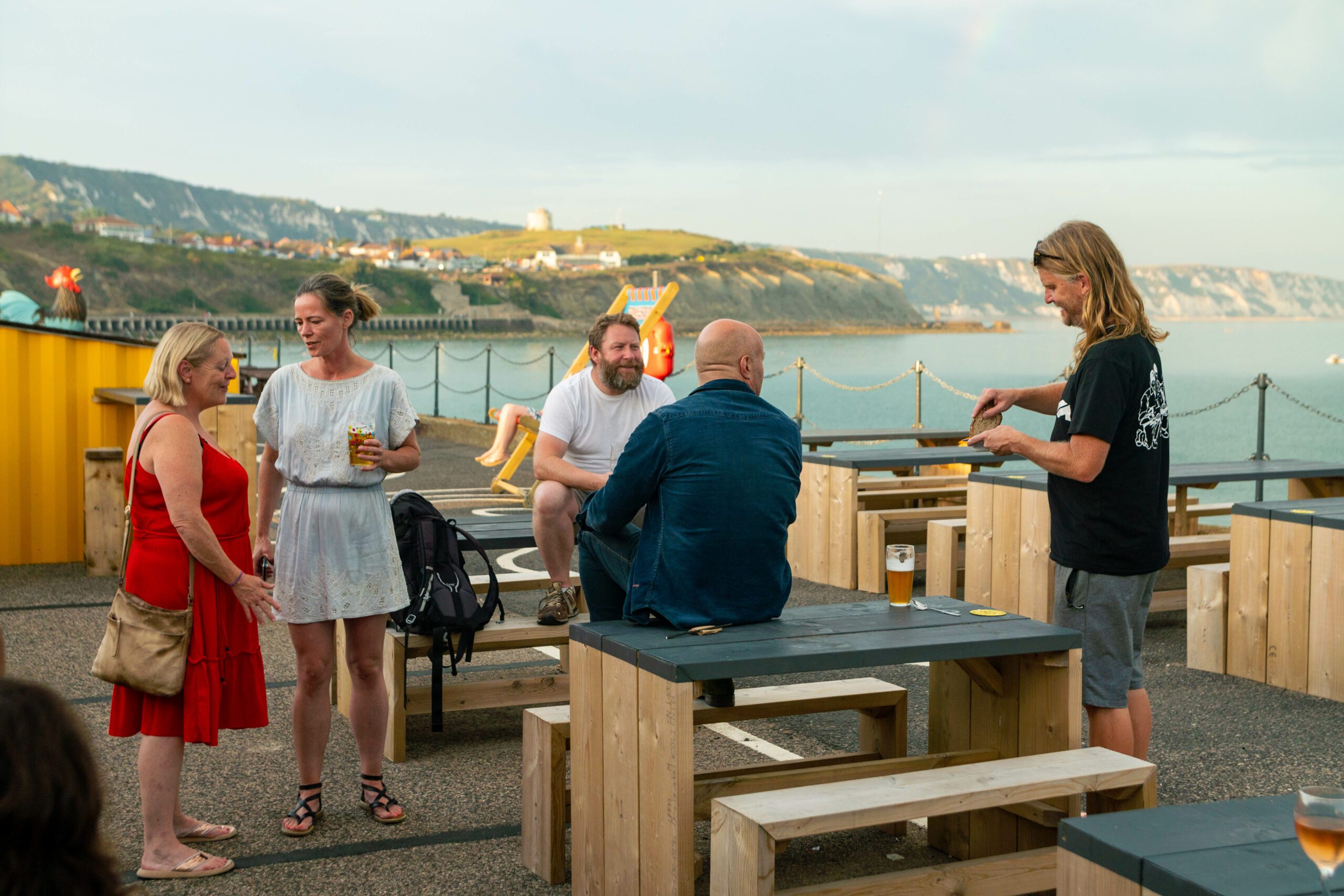 People enjoying drinks on picnic tables on the harbour arm