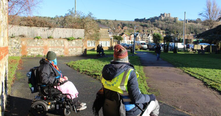 Two people in wheelchairs look out across Dover, with Dover Castle a top the hill.