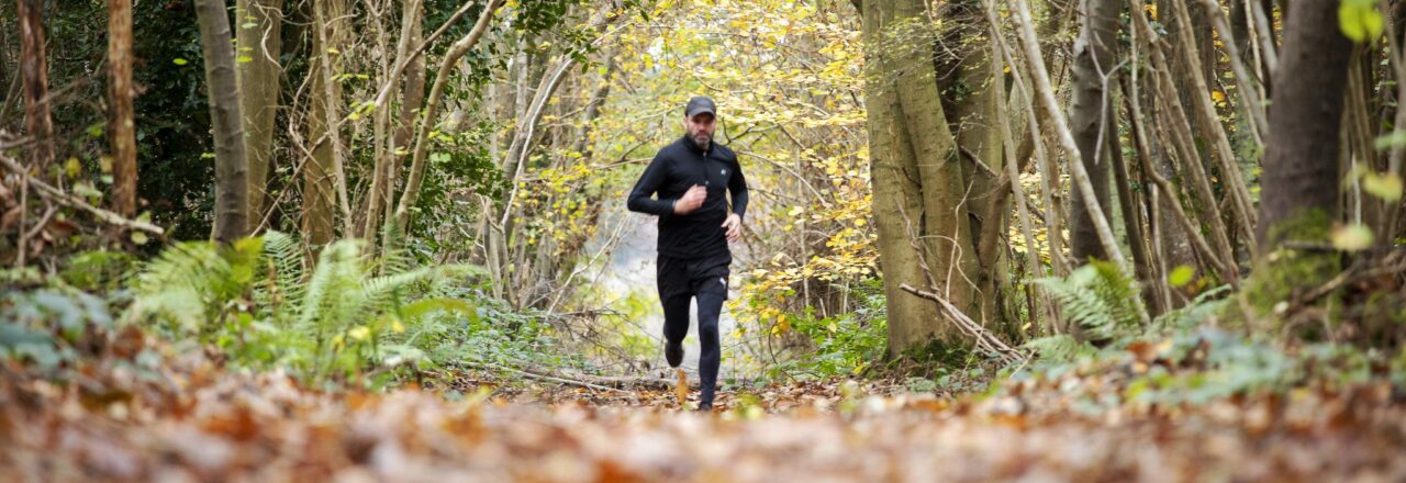 Man running along woodland path in winter with leaves on the ground