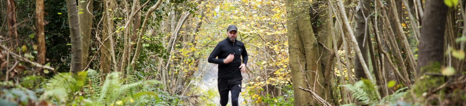 Man running along woodland path in winter with leaves on the ground