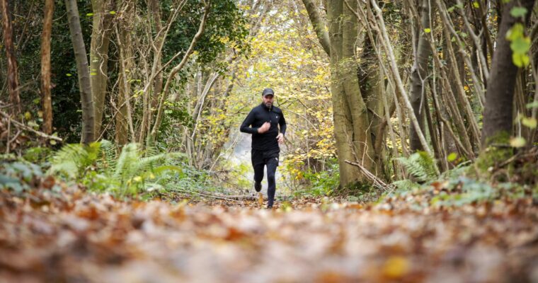 Man running along woodland path in winter with leaves on the ground