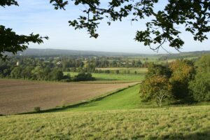  A scenic view of the Kent Downs countryside with rolling green hills, a Chevening house in distance, and a fenced pasture. 