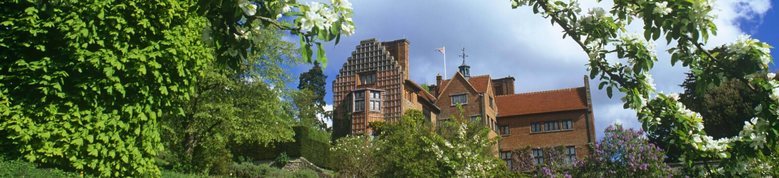 View of Chartwell from the grounds. On a sunny day, with blossom on tree in foreground.