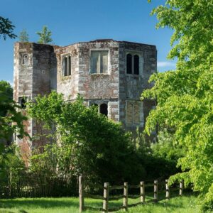 Otford Palace with weathered stone walls and arched windows, set against a cloudy sky.