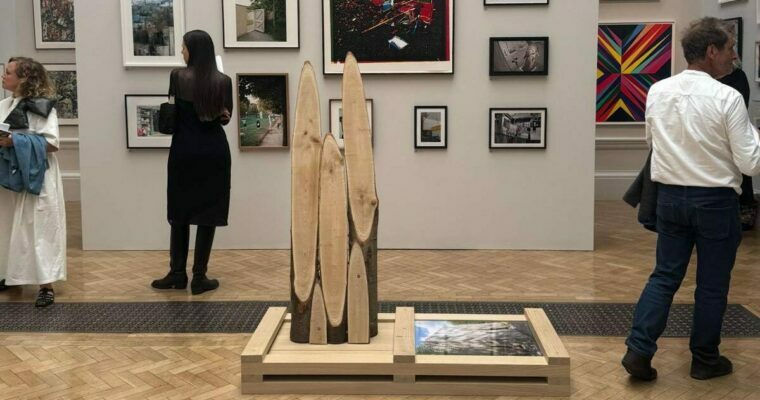 Art gallery with framed photographs, paintings, and a central wooden sculpture under soft lighting.