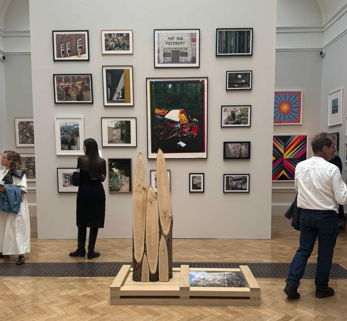Art gallery with framed photographs, paintings, and a central wooden sculpture under soft lighting.