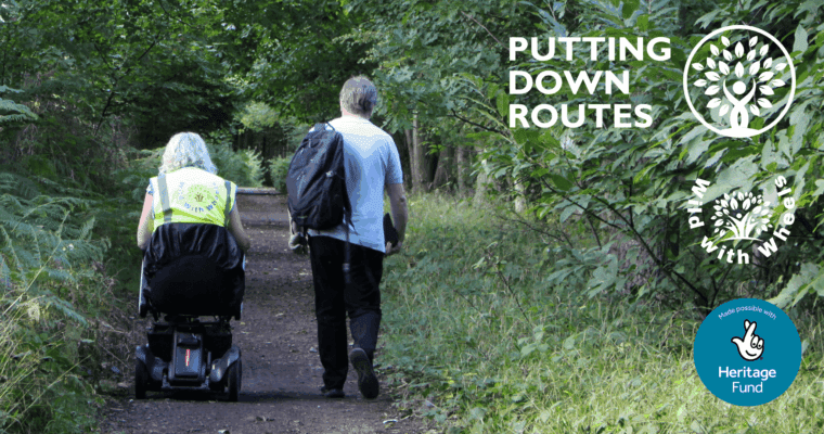 Two individuals walking on a dirt path surrounded by greenery, one using a mobility scooter.