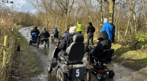 A group of people in mobility scooters navigate a gate as part of a lived experience event.