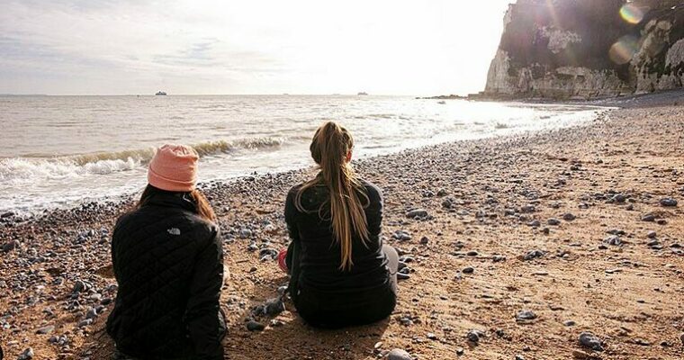 Two people sitting on beach, looking out to sea.