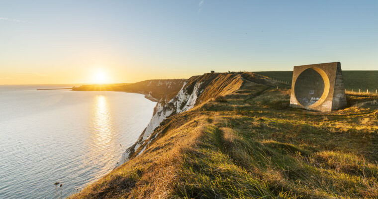 Sunset sea view across high chalk cliffs, with the sound mirror on the grass.
