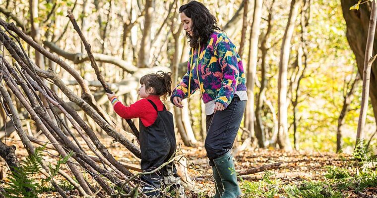 Adult and child building a den outside, in woodland. Using wooden branches.