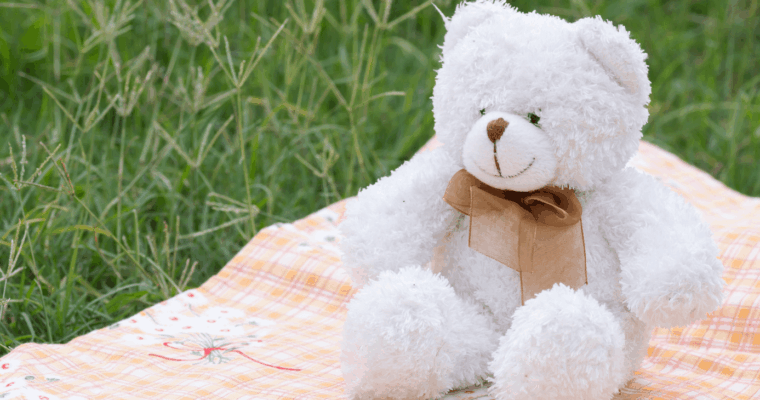 White teddy bear sitting on an orange picnic rug