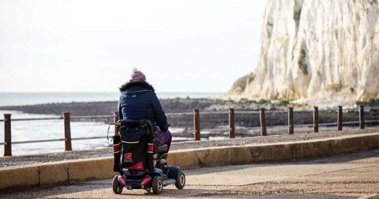 Image shows Gini Mitchell from Wild With Wheels in a motorised wheelchair on a path next to the White Cliffs of Dover