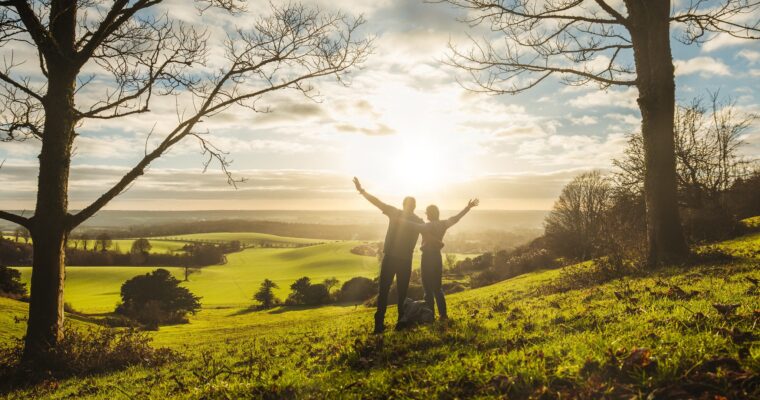 A couple with arms in the air looking at the sunset across a green landscape