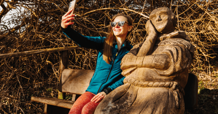 Female taking a selfie with Percy the Pilgrim, a statue on the bench